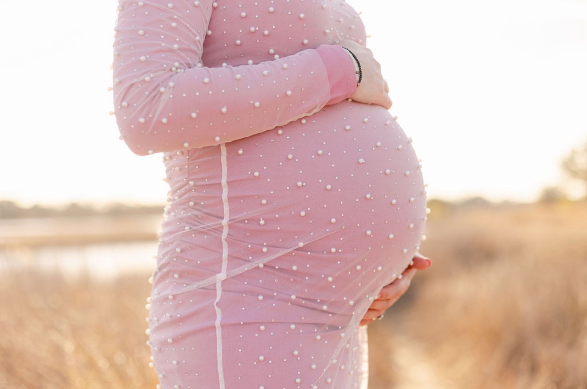 Cropped photo of baby bump. Mom is wearing a pink dress with pearls.